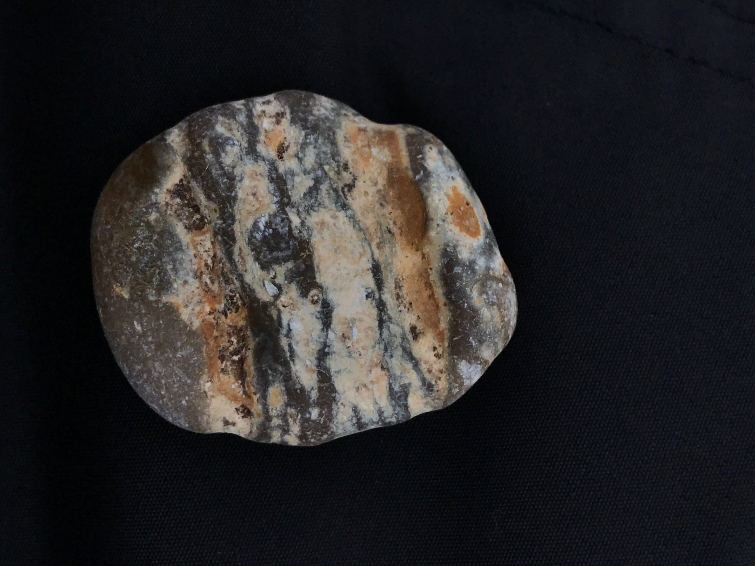 Flint nodules: photograph of a striated flint pebble with grey, orhange and cream streaks, against a black background